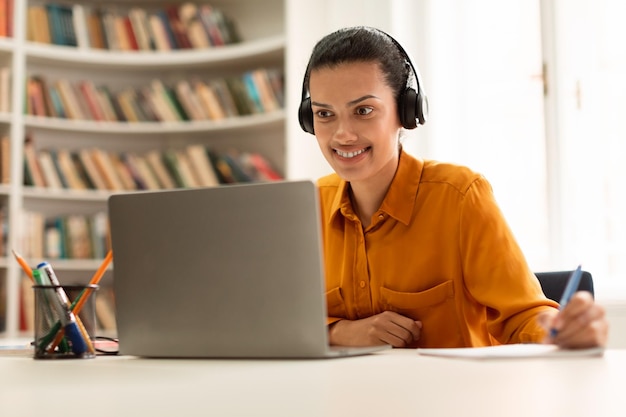happy female student learning online with laptop having remote class taking notes sitting library 116547 32562